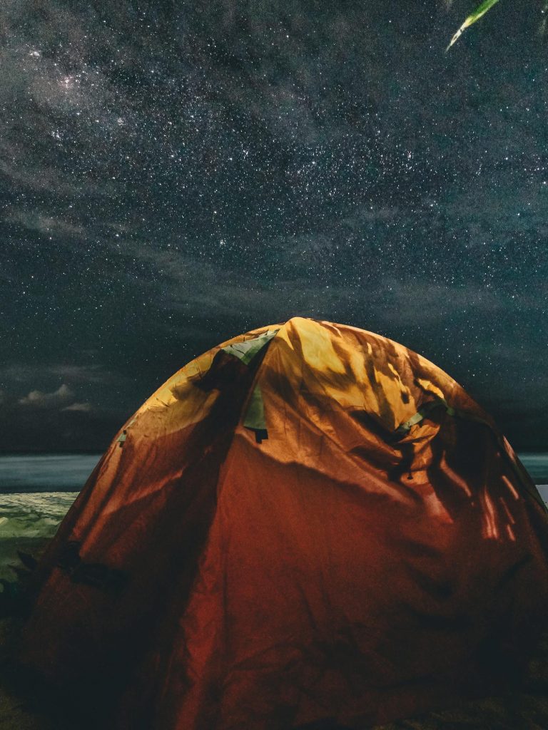 Experience the serenity of camping beneath a stunning star-filled sky with a glowing tent.